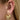 Öra med ear cuff med två guldingar och vita kristaller samt stort örhänge.