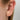 Smal ear cuff ring i guld på öra med små kulor och en vit kristall