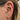 Xara threadless piercingsmycke i äkta guld med vit opalit, placerat i en traguspiercing tillsammans med andra guldsmycken.